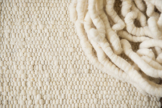 Close-up van Texelkleed Branding, samen met de garen waarvan het is geweven, gemaakt van witte Texelse schapenwol.
