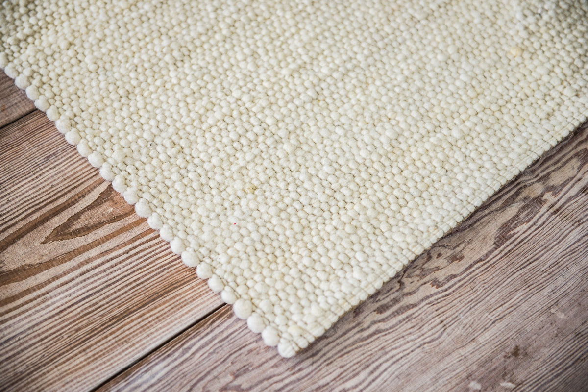Close-up van Texelkleed Branding, gemaakt van witte Texelse schapenwol, afgebeeld op een houten vloer.