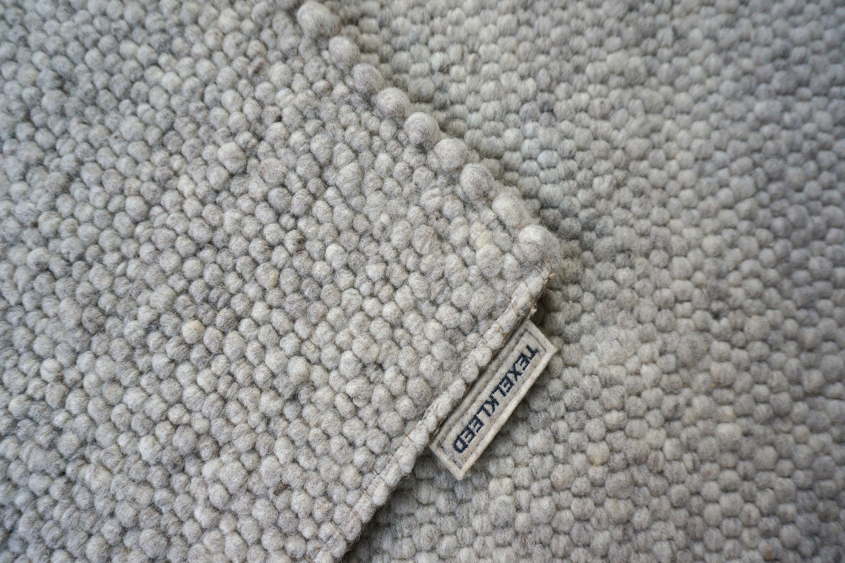 Close-up van Texelkleed Schelp, gemaakt van  80% witte Texelse en 20% blauwe schapenwol, met nadruk op de afwerking van de randen.