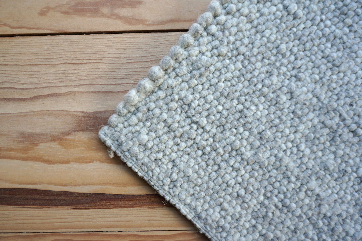 Close-up van Texelkleed Schelp, gemaakt van 80% witte en 20% blauwe Texelse schapenwol, afgebeeld op een houten vloer