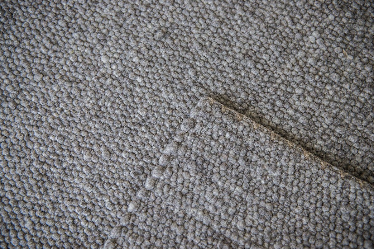 Close-up van Texelkleed Slufter, gemaakt van 50% witte  en 50% blauwe Texelse schapenwol, met nadruk op de afwerking van de randen.