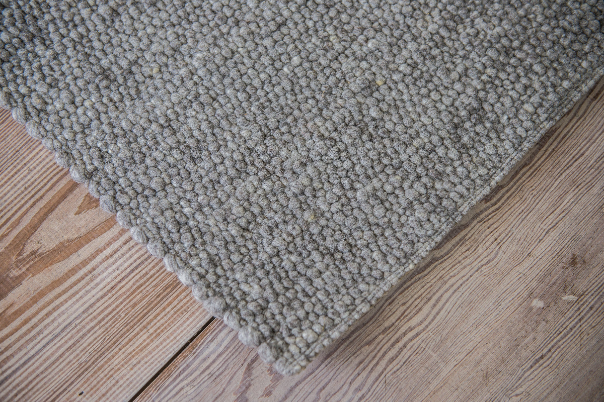 Close-up van Texelkleed Slufter, gemaakt van 50% witte en 50% blauwe Texelse schapenwol, afgebeeld op een houten vloer.