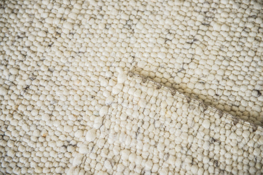 Close-up van Texelkleed Strand, gemaakt van witte Texelse schapenwol met een beetje blauw erbij, met nadruk op de afwerking van de randen.