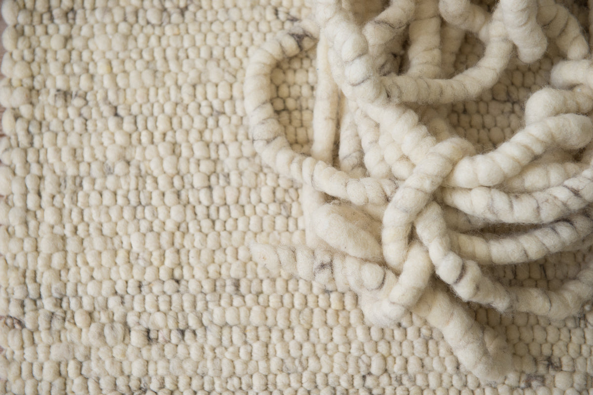 Close-up van Texelkleed Strand, samen met de garen waarvan het is geweven, gemaakt van witte Texelse schapenwol met een beetje blauw erbij.