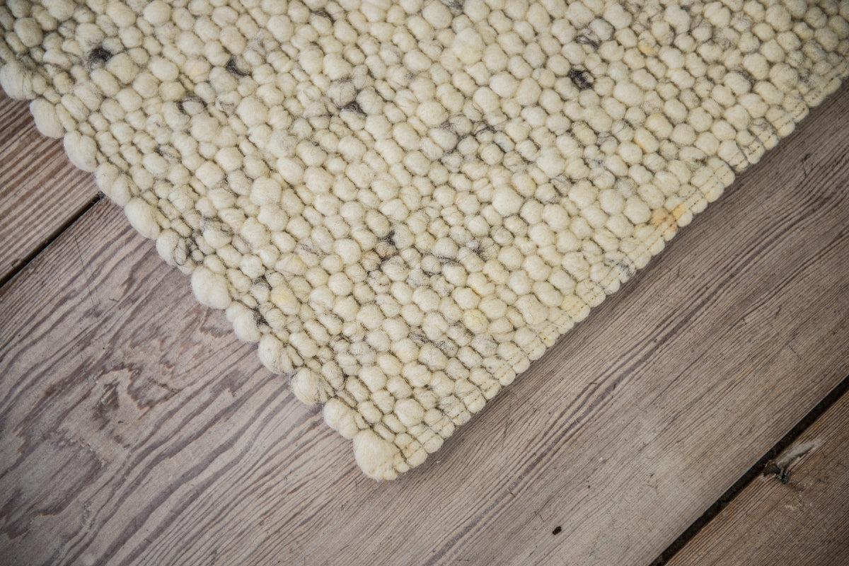 Close-up van Texelkleed Strand, gemaakt van witte Texelse schapenwol met een vleugje blauw erbij, afgebeeld op een houten vloer.